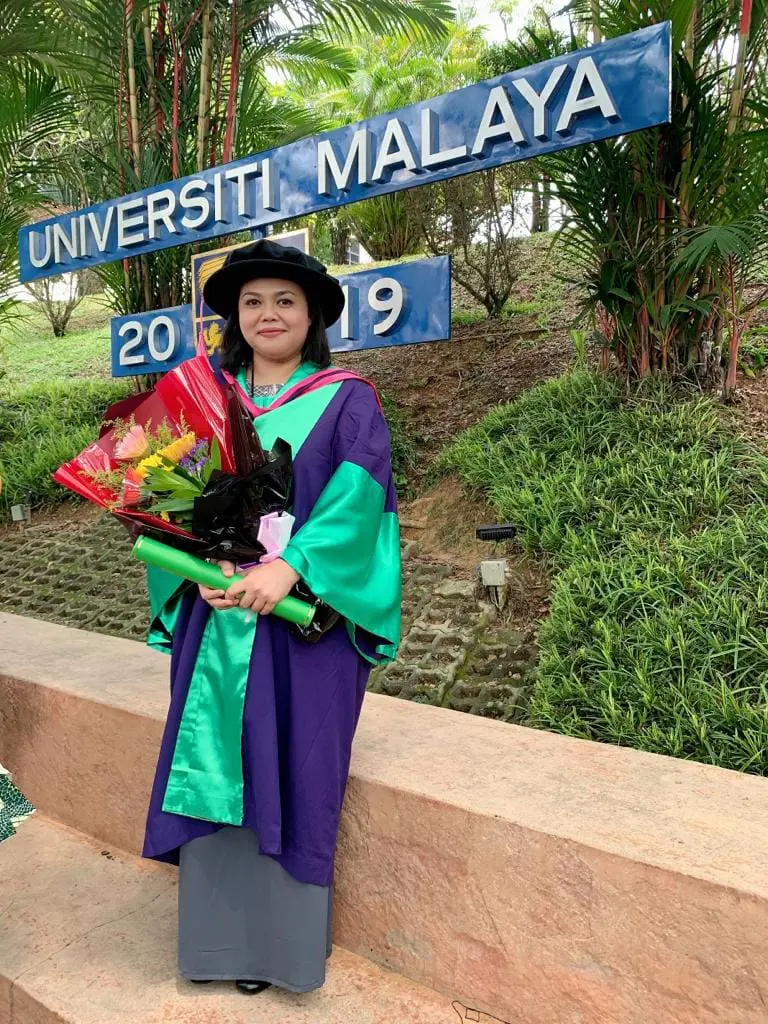  Dr. Norashikin Mohd Shaharuddin  in grad robe posing in front of University Malaysa signage 