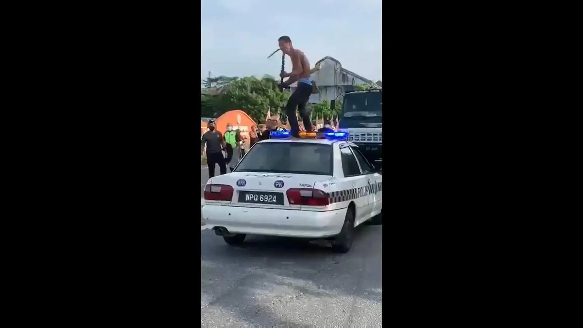 Man runs amok, swinging a parang while standing on top of a police car