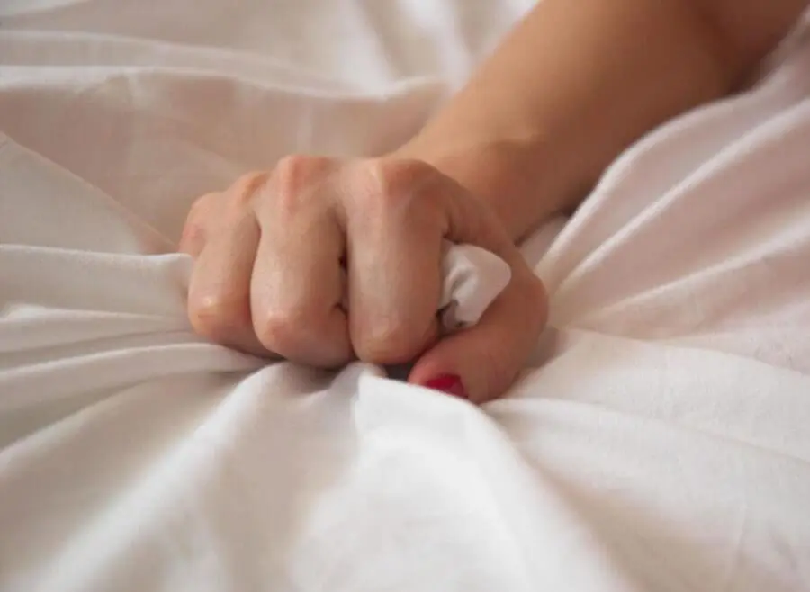 Hand gripping on a fabric, most likely a sheet or blanket.