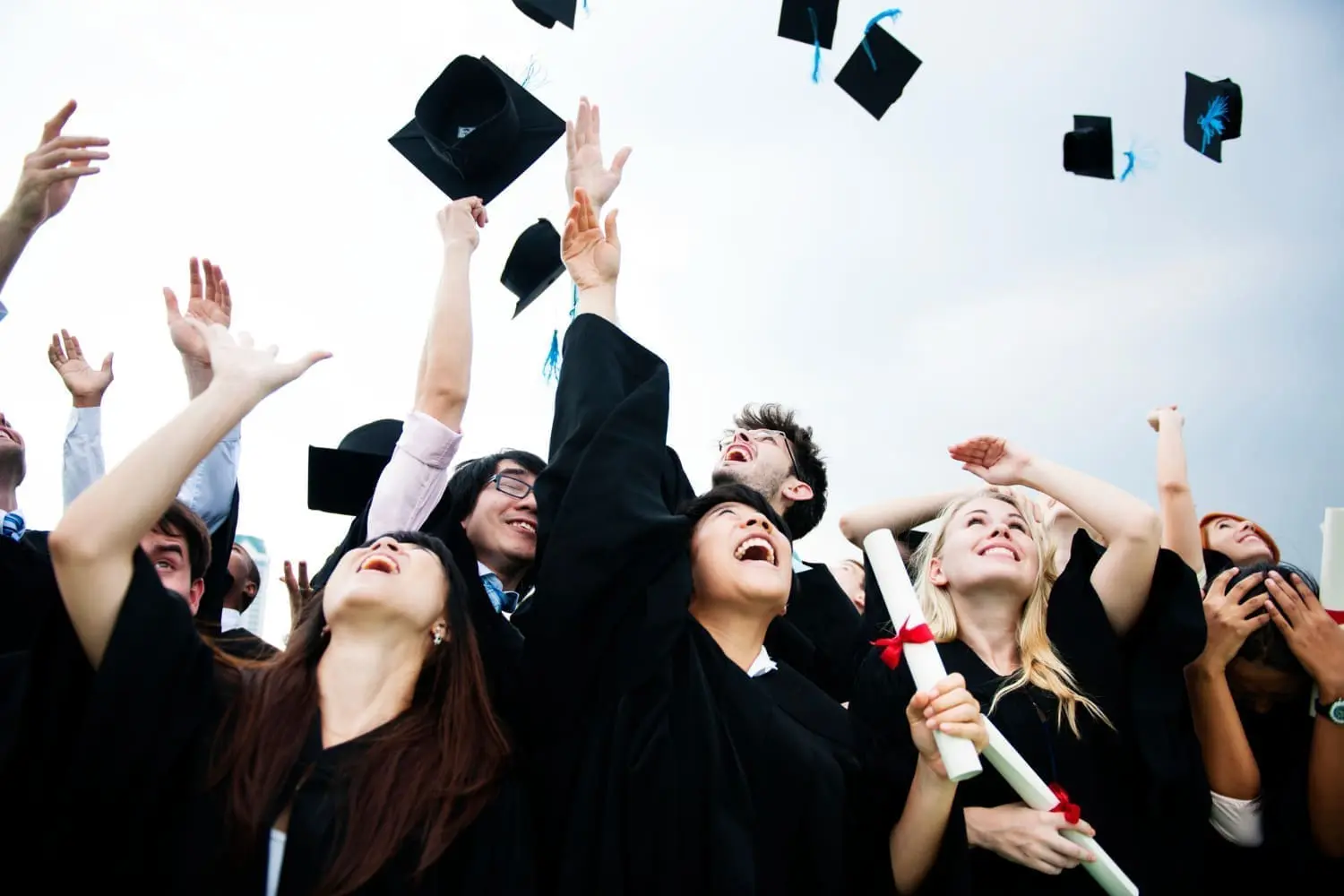 group-diverse-grads-throwing-caps-up-sky