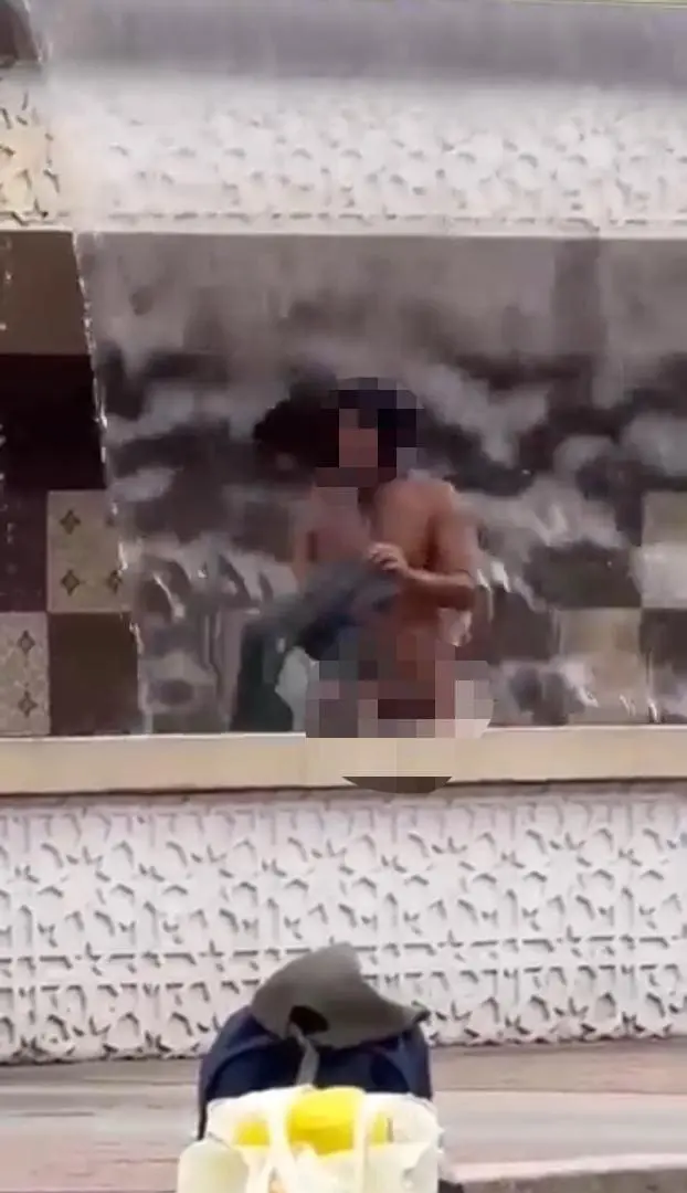 homeless man washing clothes in a fountain at kl