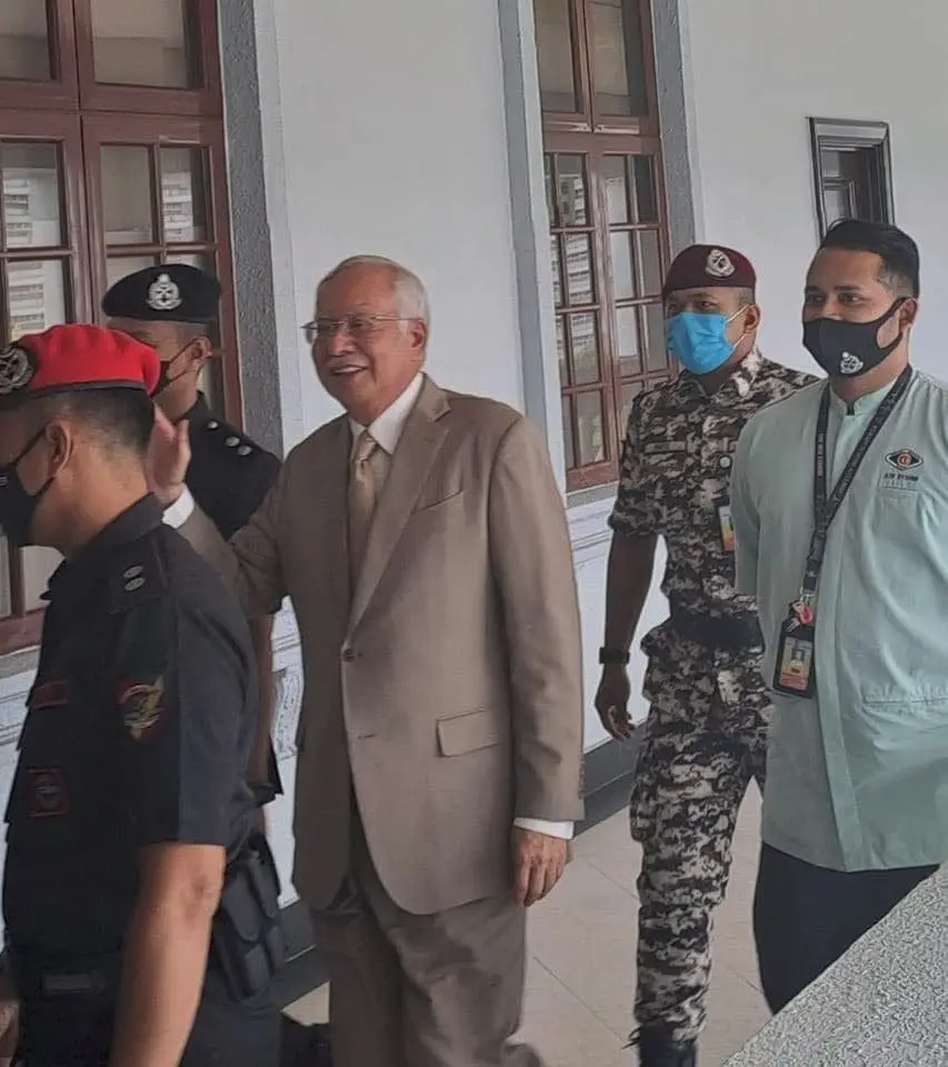 Najib Razak smiling and waving outside the courtroom