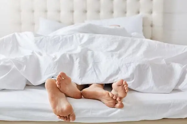 Two pairs of feet rubbed together on a bed