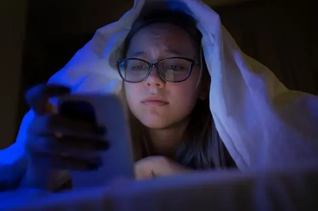 A woman using her phone at night under her blanket