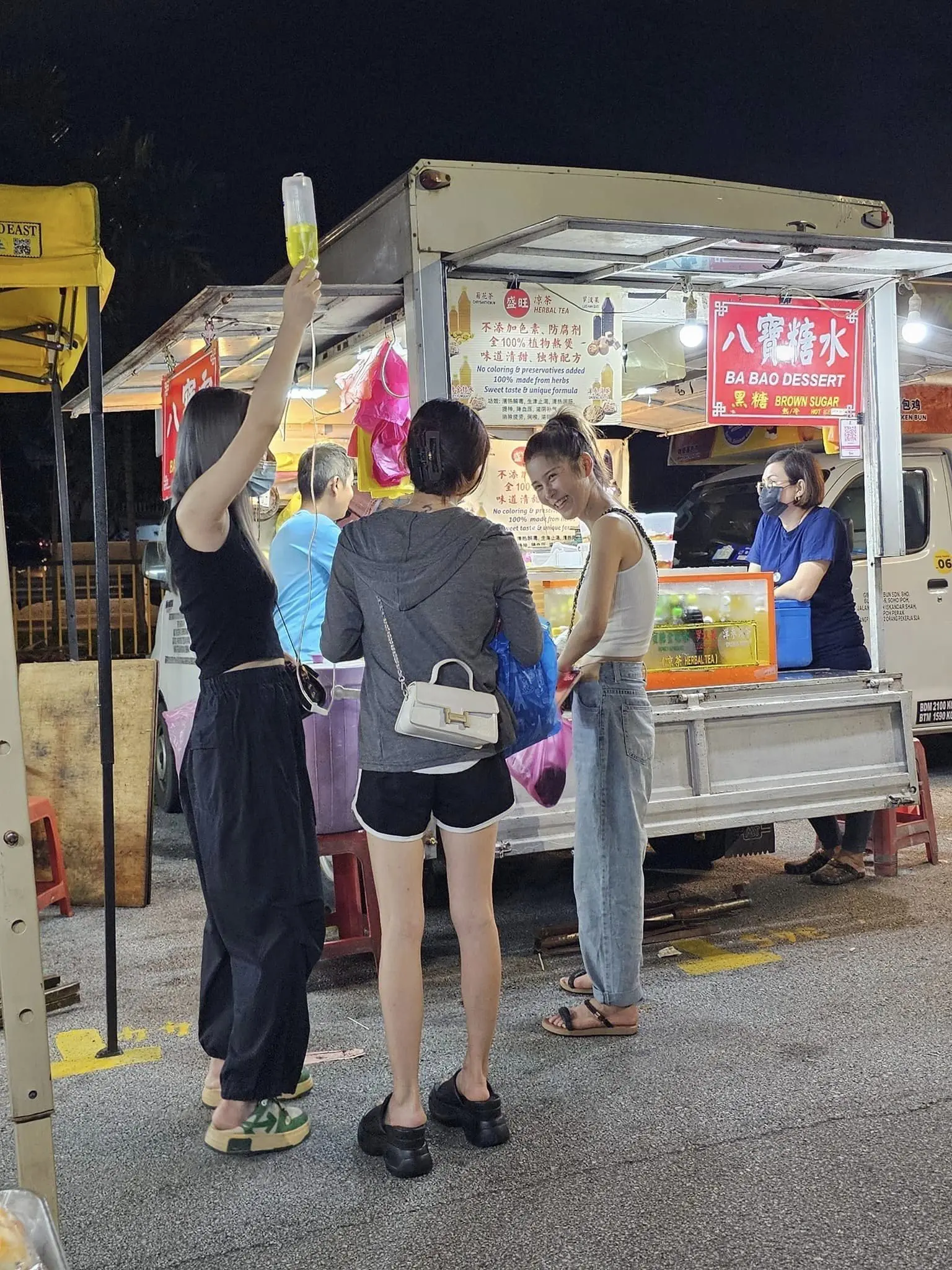 Woman visits dessert stall at Taman Connaught night market along with IV drip