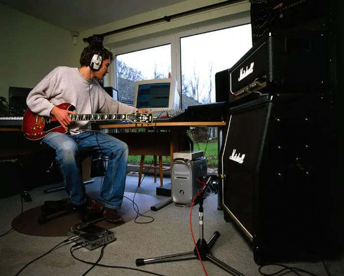 Caucasian man listening to his headphones with a guitar in his hand, equipped with Marshall devices around him.