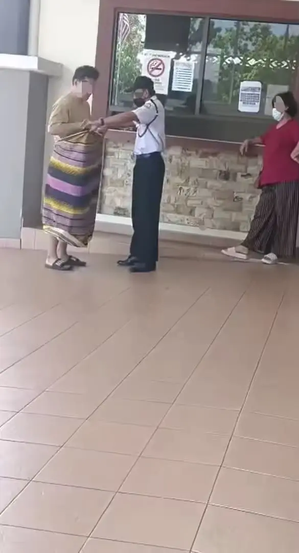 Guard helping M'sian man wear a sarong