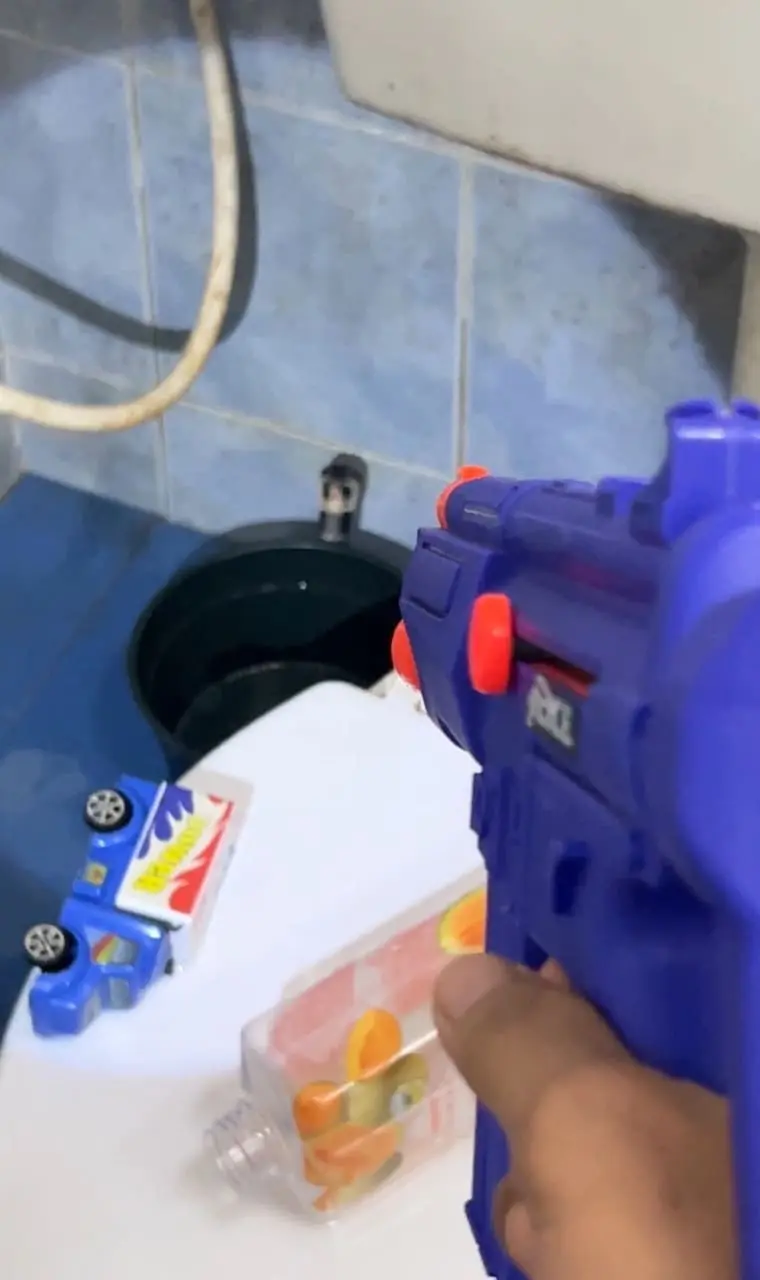 man playfully confronts snake with a toy gun in toilet