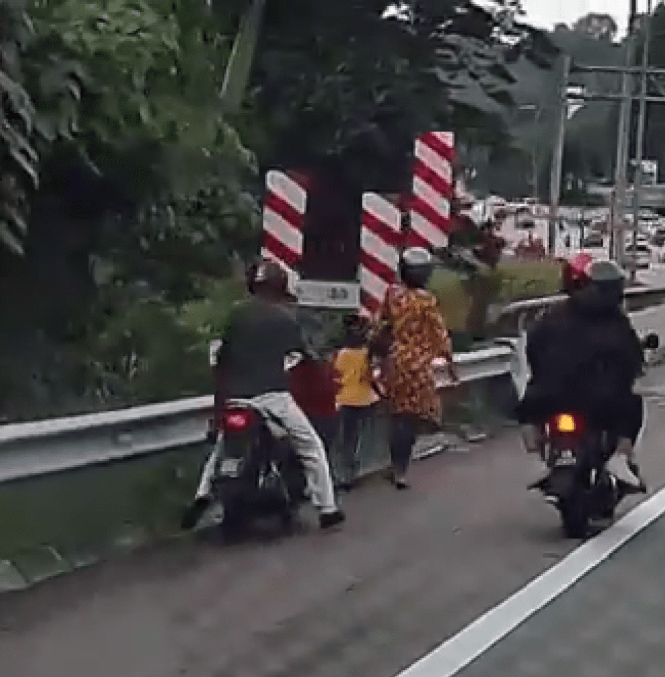 man psuhing his motorbike on a highway while his wife and kid walking infront