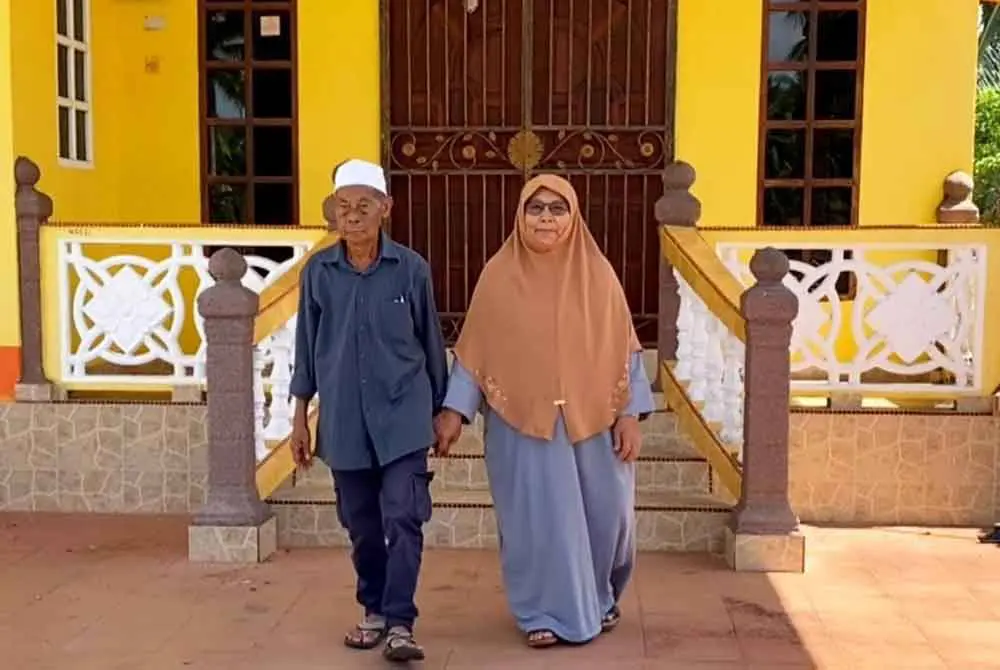 msian elderly couple standing infront of their house