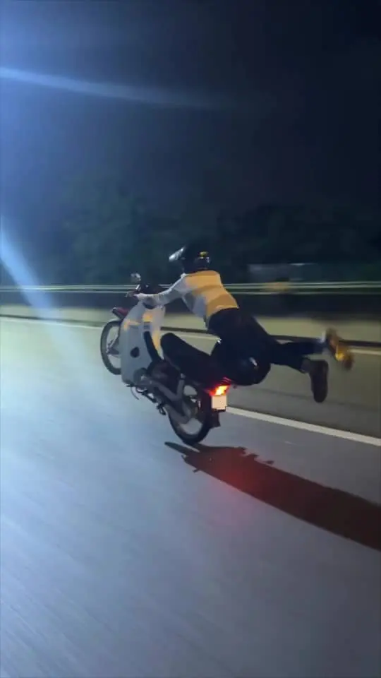 msian man performing dangerous wheelie stunt on road