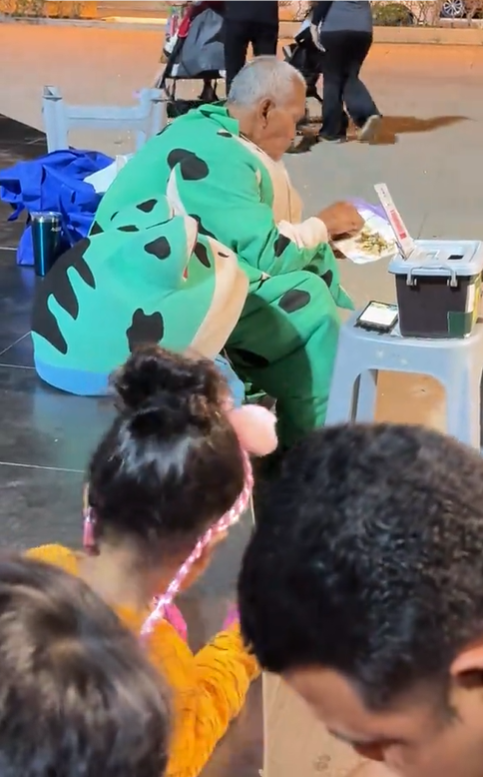 Old man in frog mascot costume eating his meal