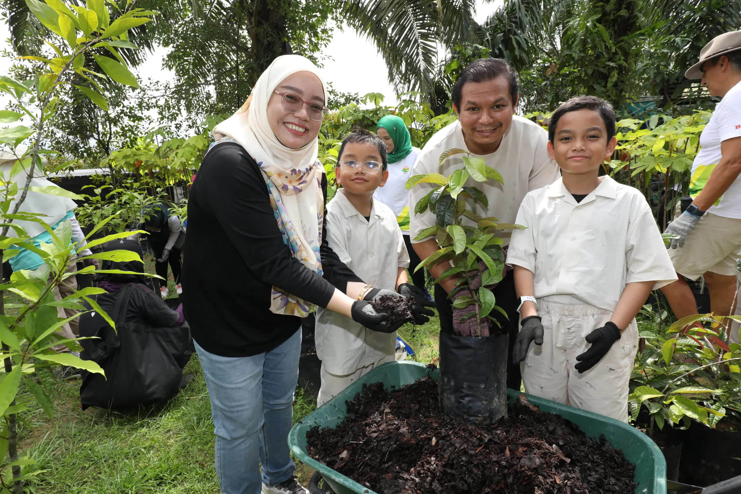 Saiful and Adawiyah adding mulch to a plant together with their children