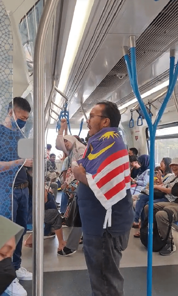 a msian with flag on his shoulder singing national song on mrt