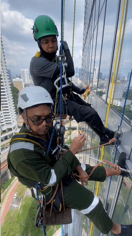 Two msian men hanging out onto rope outside a buliding while eating buns