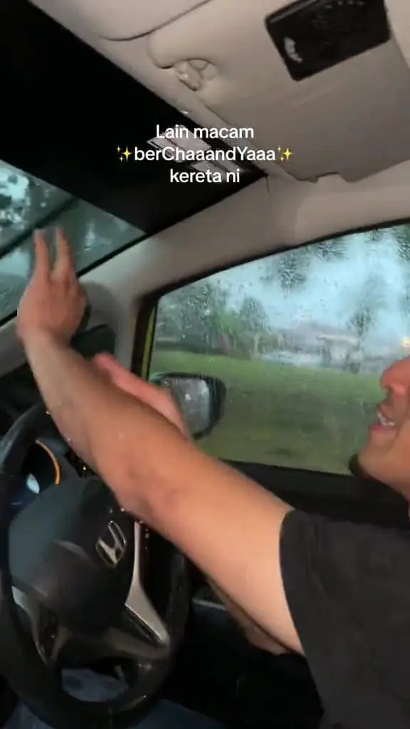 msian man playing with the water that is dripping from his car front windshield.
