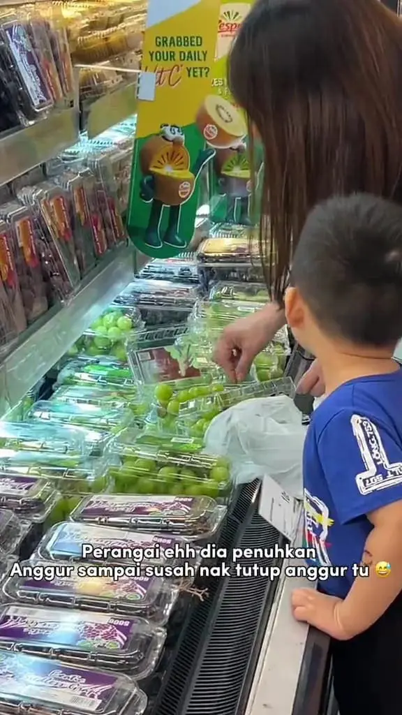 A Malaysian woman fills up her box by putting more grapes in it from other boxes.