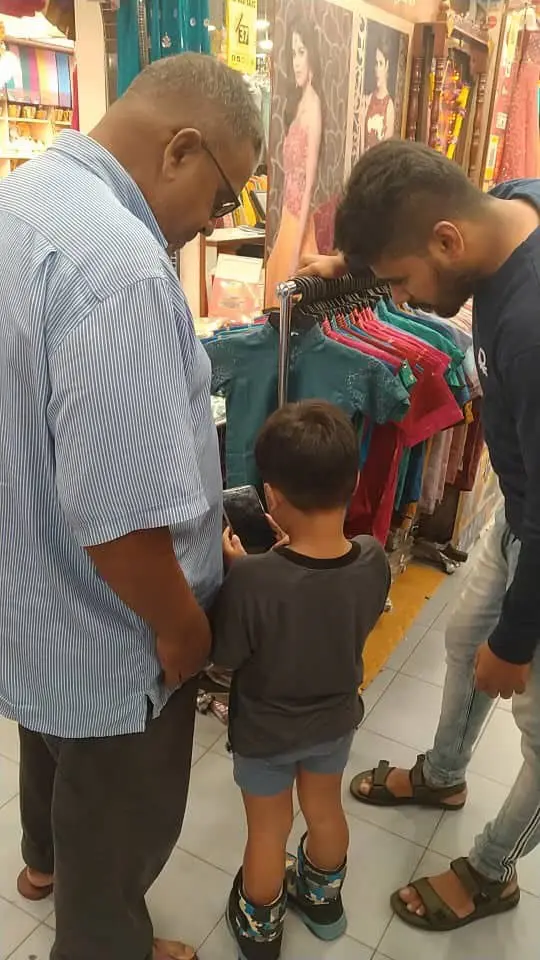 Muhammad Nurhaq, along with his grandfather, looking through Indian traditional clothes at a clothing store.