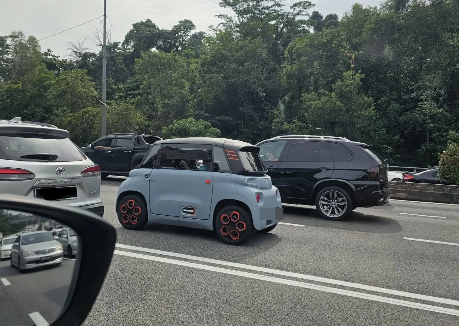 A man driving a 2-seater blue Citroen Ami on a road at Jalan Duta.