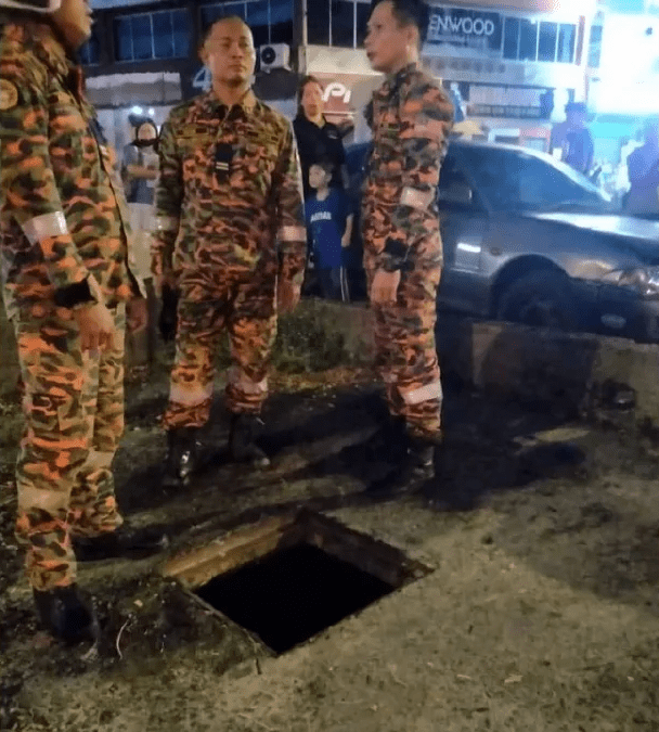 Firefighters standing near manhole which boy fell into