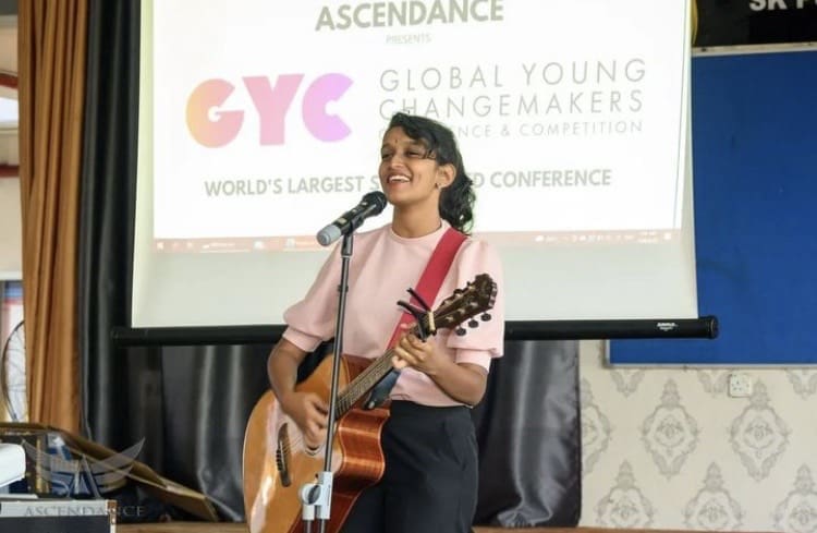 Heerraa Ravindran singing on stage while playing a guitar