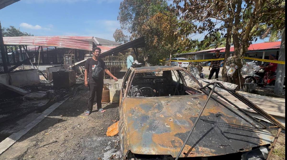 man standing beside a burnt car