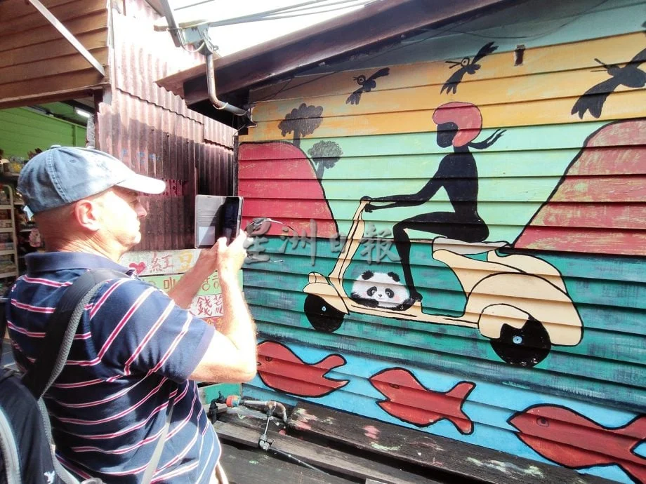 Man taking photograph of mural at Chew Jetty