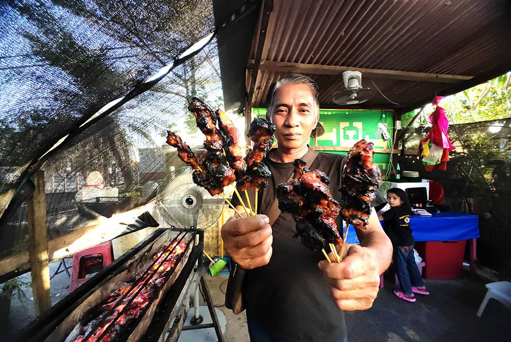 msian man showing sticks of chicken satay