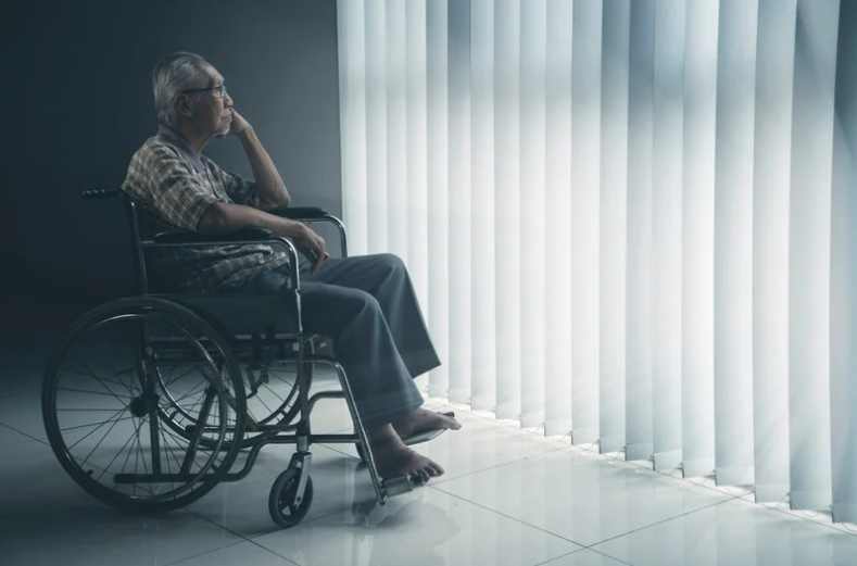 Old man sitting on wheelchair while looking at window