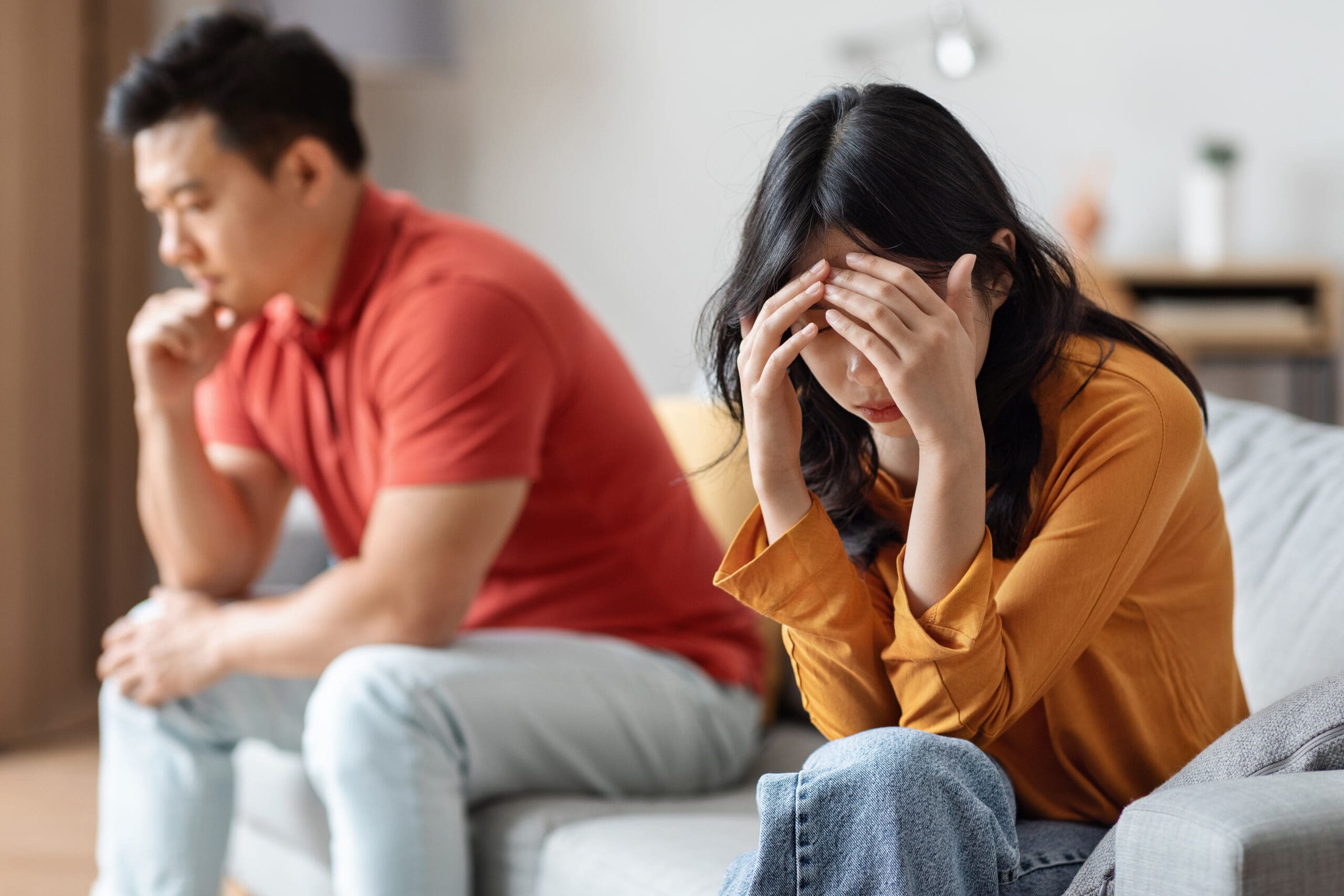 Sad Asian couple sitting on sofa